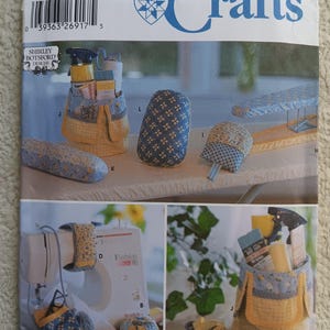 May include: Simplicity Crafts sewing pattern featuring various craft projects. The pattern includes instructions for a sewing machine cover, a spray bottle holder, and other accessories. The cover and holder are yellow and blue.