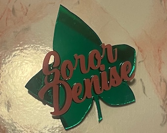 Può includere: Un ornamento in acrilico a forma di foglia verde con le parole "Soror Denise" scritte in rosa.