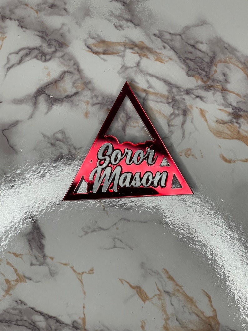 K&ouml;nnte beinhalten: Ein roter, dreieckiger Schl&uuml;sselanh&auml;nger aus Acryl mit der Aufschrift "Soror Mason" in wei&szlig;en Buchstaben.