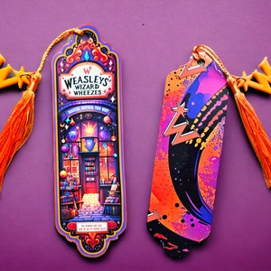 Puede incluir: Dos marcadores de libros coloridos con borlas naranjas. Un marcador presenta una ilustración caprichosa de la tienda Weasley's Wizard Wheezes con el texto "Magical Mayhem This Way". El otro marcador tiene un diseño abstracto negro, naranja y morado con rayos.