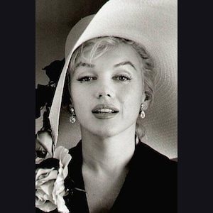 May include: A black and white portrait of a woman wearing a large, wide-brimmed hat and a dark dress. She is looking directly at the camera with a soft smile.