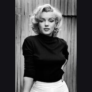 May include: A black and white portrait of a woman with blonde hair wearing a black turtleneck sweater and a white skirt.