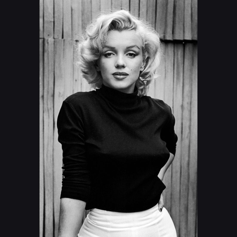 May include: A black and white portrait of a woman with blonde hair wearing a black turtleneck sweater and a white skirt.