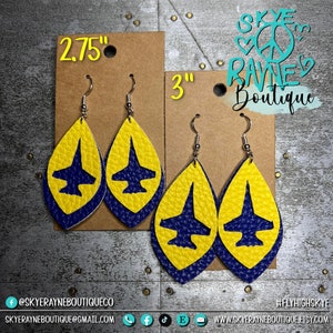 May include: A pair of blue and yellow leather earrings with a silhouette of a jet fighter plane. The earrings are available in two sizes: 2.75 inches and 3 inches. The earrings are handmade and are perfect for anyone who loves aviation.
