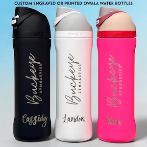 May include: Three Owala water bottles in black, white, and neon pink, each featuring a flip-top lid and the text CUSTOM ENGRAVED OR PRINTED OWALA WATER BOTTLES at the top. Each bottle is personalized with the text Buckeye Gymnastics and a name.