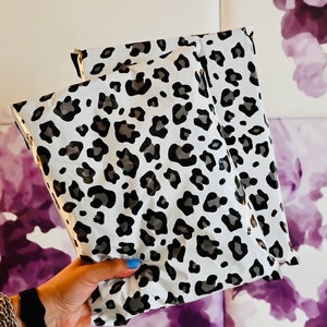 May include: Two white and black leopard print mailing envelopes. The envelopes are folded and stacked on top of each other.