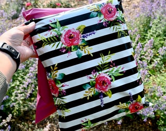 May include: A floral-patterned shipping mailer with a black and white striped background. The design features watercolor-style pink roses, green leaves, and purple accents. The interior of the mailer is a bright pink color.