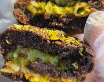 May include: Close-up of a chocolate brownie cookie with a green pistachio filling. The cookie is split in half, revealing the filling. The text "keto me" is visible on the bottom of the image.