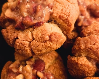 Op de afbeelding: Close-up van een stapel goudbruine koekjes met een zoete, nootachtige topping. De koekjes zijn licht gebarsten en hebben een zachte, kauwbare textuur. De topping is een mengsel van noten en karamel, en het is gelijkmatig over de koekjes verdeeld.