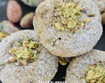 May include: Close-up of three pistachio cookies, dusted with powdered sugar and topped with chopped pistachios. The cookies are stacked on top of each other, and the text "keto me every bite, a healthy delight" is visible at the bottom of the image.