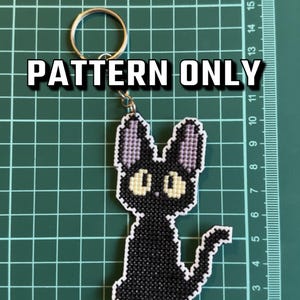 May include: A cross-stitch pattern for a black cat with yellow eyes and purple ears. The pattern is on a white background and is ready to be stitched.