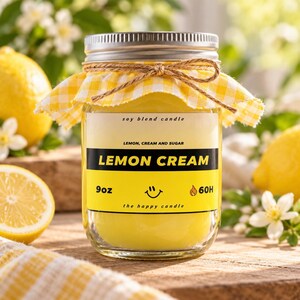 May include: A 9oz soy blend candle in a glass jar with a silver lid, topped with a yellow and white gingham fabric cover tied with twine. The label reads Lemon Cream, Lemon, Cream and Sugar, 9oz, 60H, and the happy candle with a smiley face.