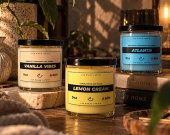 May include: Three glass jar candles with black lids. The left candle is white labeled Vanilla Vibes, the center is yellow labeled Lemon Cream, and the right is blue labeled Atlantis. Each 9oz soy blend candle features a smiley face icon and 60H text.