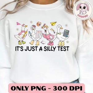May include: White sweatshirt with a whimsical design featuring cartoon geese dressed as students. The geese are holding school supplies and books, with the text "IT'S JUST A SILLY TEST" below. The bottom of the image has the text "ONLY PNG - 300 DPI".