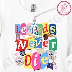 May include: White sweatshirt with a colorful graphic that reads "Legends Never Die." The design includes baseball bats, a glove, a baseball, a trophy, and a baseball cap. The text is in various colors and fonts.