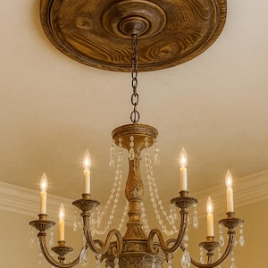 May include: Ornate, antique-style chandelier with six candle-shaped lights and crystal accents. The fixture is suspended from a decorative wooden ceiling medallion. The chandelier has a bronze finish and is a classic lighting fixture.