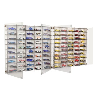 Puede incluir: Una vitrina de acrílico blanco con múltiples estantes para guardar y exhibir coches de juguete. La vitrina tiene puertas transparentes y está llena de filas de coches de juguete coloridos.