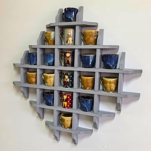 May include: A gray wooden wall shelf with a heart shape design. The shelf has multiple compartments to display mugs. The mugs are various colors and patterns, including blue, yellow, red, and white.