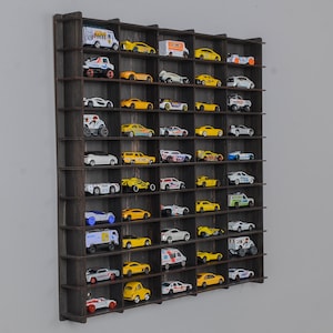 Op de afbeelding: Een zwarte houten wandplank met 48 individuele vakken om speelgoedauto's te presenteren. De plank is gevuld met een verscheidenheid aan speelgoedauto's in verschillende kleuren, waaronder geel, rood, blauw en wit.