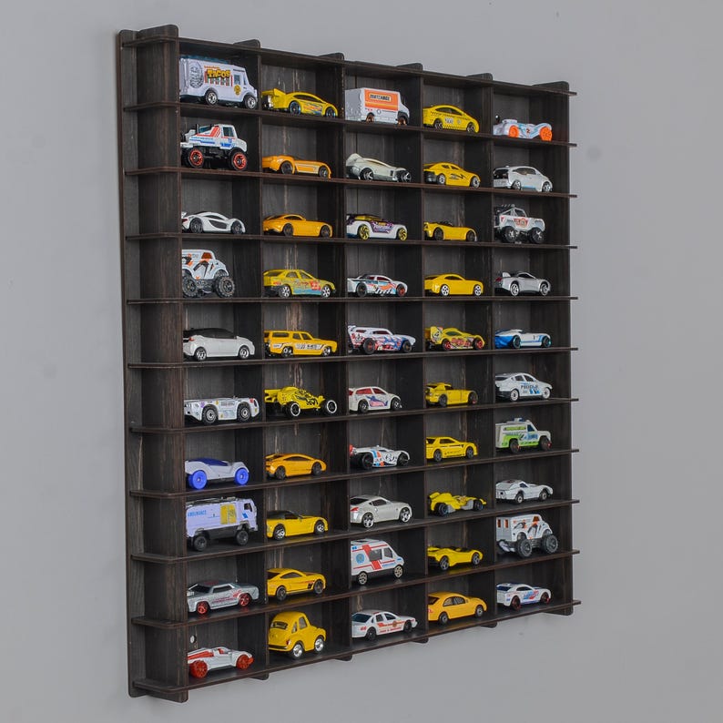 Op de afbeelding: Een zwarte houten wandplank met 48 individuele vakken om speelgoedauto's te presenteren. De plank is gevuld met een verscheidenheid aan speelgoedauto's in verschillende kleuren, waaronder geel, rood, blauw en wit.