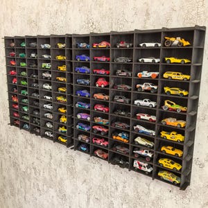 Op de afbeelding: Een zwarte houten displayplank met meerdere vakken om speelgoedauto's op te bergen. De plank is gevuld met een verscheidenheid aan kleurrijke speelgoedauto's, waaronder rode, blauwe, gele en groene.