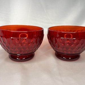 May include: Two red glass bowls with a diamond pattern. The bowls have a footed base.