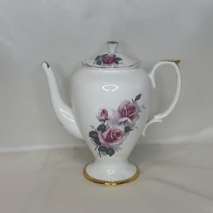 May include: White porcelain teapot with a lid, decorated with pink and green rose motifs. The teapot has gold trim on the base, handle, and spout. The lid also features a rose design and gold trim. A classic item for a tea set.