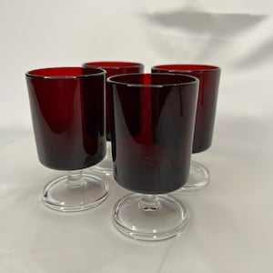 Può includere: Set di quattro bicchieri da shot con gambo in vetro trasparente con corpo di colore rosso scuro, quasi bordeaux.