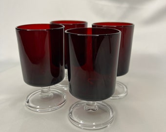 May include: Set of four clear glass stemmed shot glasses with a dark red, almost burgundy, colored body.