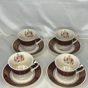 Puede incluir: Juego de cuatro tazas de té y platillos vintage con un diseño floral. Las tazas y los platillos son blancos con un borde marrón y dorado. El diseño floral presenta flores rosas, rojas y azules.