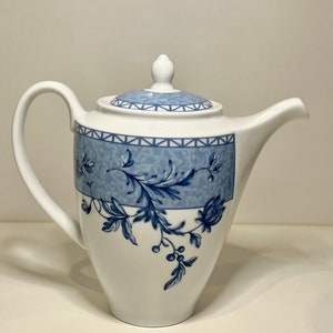 Könnte beinhalten: Eine weiße Teekanne aus Keramik mit einem blauen Blumendesign und einem Deckel. Die Teekanne hat einen Henkel und einen Ausguss.