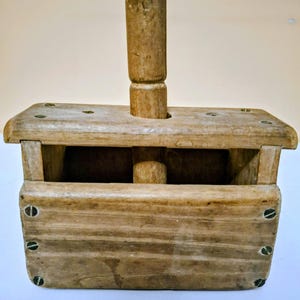 May include: A vintage wooden butter mold, rectangular in shape, with a tall, cylindrical handle. The box is assembled with visible screws and contains a small, round wooden piece. The wood has a natural, aged appearance.