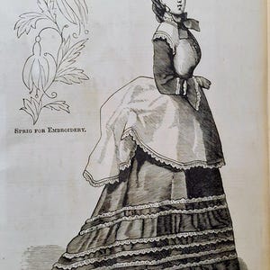 May include: A black and white line drawing of a person wearing a long dress with a ruffled skirt, a high-collared bodice, and a bustle. To the left, a floral design is labelled with the text Sprig for Embroidery in black capital letters.