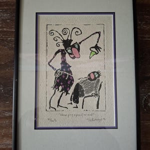 May include: Framed art print featuring a whimsical, black and purple figure with a long tongue and a seated figure in a striped shirt. The print includes the text "Worm giving a piece of her mind" and is signed and numbered.