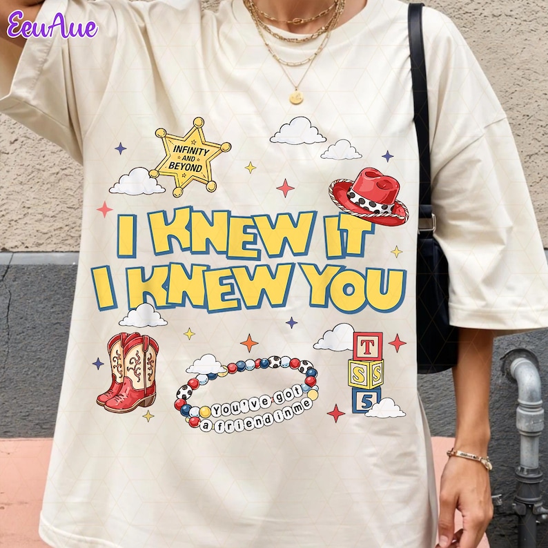 May include: A cream-colored t-shirt featuring a graphic print with the text I KNEW IT I KNEW YOU, a yellow sheriff star badge labeled INFINITY AND BEYOND, a red cowboy hat, red cowboy boots, a beaded bracelet with the text You've got a friend in me, and blocks.
