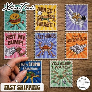 May include: A selection of embroidered patches with diverse designs and text. The patches showcase images of a hamburger, an astronaut, a crab with tools, a spaceship, and other quirky illustrations. Each patch has a postage stamp-like border.