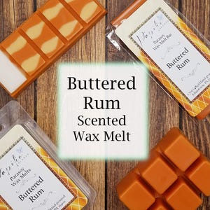 May include: Overhead shot of buttered rum scented wax melts. The image features several orange wax melt bars and cubes, some with a lighter yellow design. One bar is in a clear package with the text "Buttered Rum".