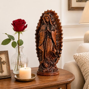 May include: A brown, textured resin statue of the Virgin of Guadalupe featuring a radiant sunburst halo and a small cherub at the base. The figure is depicted with hands clasped in prayer, wearing a long, flowing robe with intricate folds.