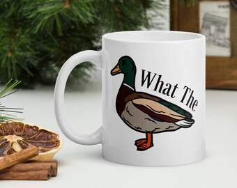 May include: White ceramic coffee mug with a cartoon image of a duck and the text "What The" printed on it.
