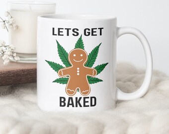 May include: White ceramic mug with a gingerbread man inside a green marijuana leaf. The text "Lets Get Baked" is printed on the mug.
