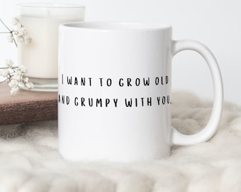 May include: White 11oz ceramic mug with the text "I WANT TO GROW OLD AND GRUMPY WITH YOU." The mug has a curved handle and is designed on both sides. A candle and flowers are in the background.
