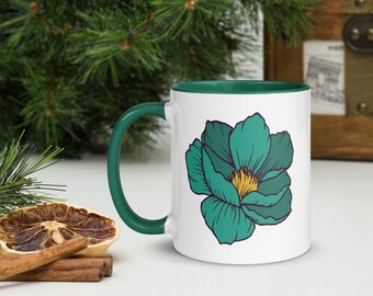 May include: White ceramic mug with a green rim and handle. The mug features a teal blue flower with a yellow center.