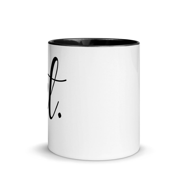 May include: White ceramic mug with a black rim and handle. The mug has the word "Just" written in black cursive on the front.
