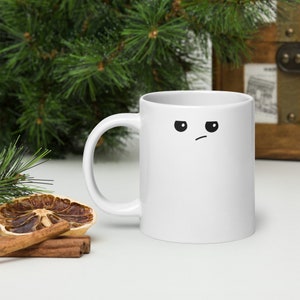 May include: White ceramic coffee mug with a simple black line drawing of a frowning face.