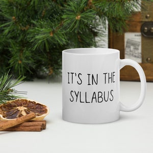 May include: White ceramic coffee mug with black text that reads "IT'S IN THE SYLLABUS".