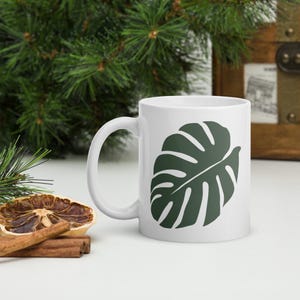 May include: White ceramic mug with a green monstera leaf design.