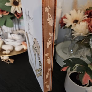 May include: A hardback book titled "My Book of Bones" with a white cover and an orange spine. The spine has a repeating floral pattern. The cover features a skeleton illustration and handwritten text.
