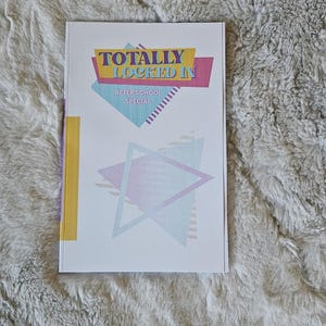 May include: A white rectangular book cover featuring the text TOTALLY LOCKED IN and AFTER SCHOOL SPECIAL in blue and purple. The design includes geometric shapes in pastel pink, blue, and yellow, with a vertical yellow stripe on the left side.
