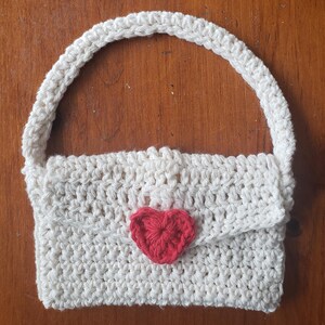 May include: A small white crocheted handbag with a red heart-shaped embellishment.