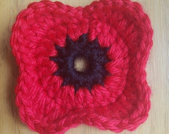 May include: A red crocheted poppy flower with a black center. The flower is made with yarn and has a textured surface.